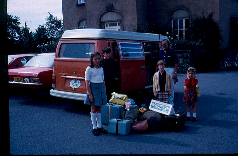 family with their luggage standing by their orange camper