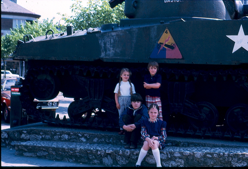 four kids in front of a tank